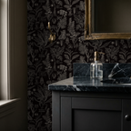 Charcoal botanical wallpaper in elegant bathroom setting with gold mirror.