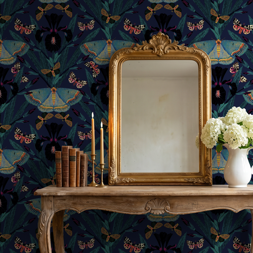 Moody navy wallpaper with moths and irises behind ornate mirror and candles.