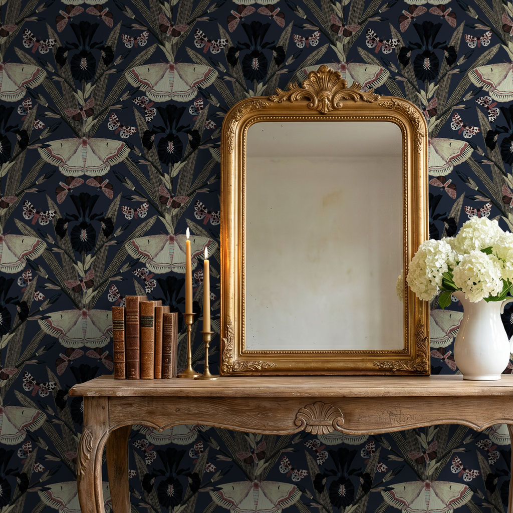 Navy wallpaper with moths and irises behind ornate mirror and wooden table.