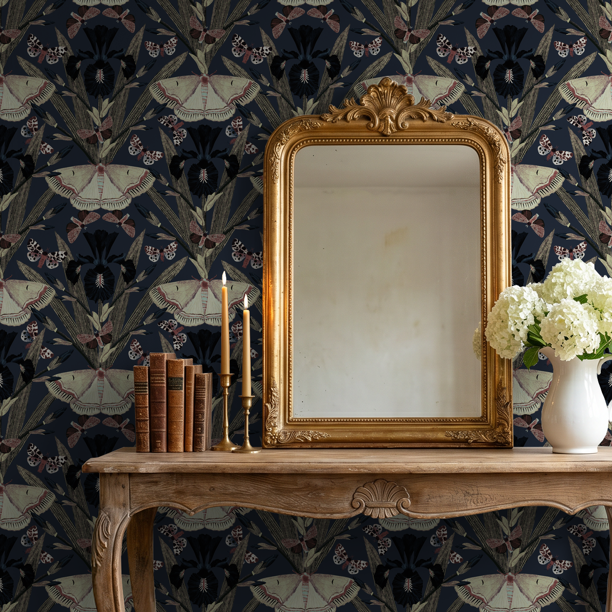 Navy wallpaper with moths and irises behind ornate mirror and wooden table.